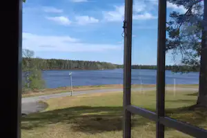 Blick vom Fenster auf Seeufer, Rasenfläche und einen geschwungenen Weg am Campingplatz, im Hintergrund Wald.