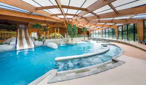 Schwimmbecken im überdachten Bereich mit Holzpergola, Liegen und Glasfront, daneben Sitzstufen und Wasserfläche.