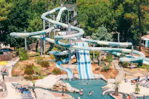Wasserrutschen und ein türkisfarbenes Schwimmbecken in einem Campingpark, umgeben von Bäumen und Liegen.