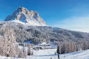 Bergpanorama mit verschneiten Wäldern und einem Campingplatz im Tal, Skifahrer auf der Piste vor den Häusern.