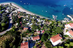 Luftaufnahme eines Campingplatzes am Strand mit Wohnwagen, Wegen und Booten im türkisfarbenen Meer.