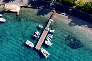 Luftaufnahme vom Campingplatz am See mit Stegen und mehreren Booten im klaren, türkisfarbenen Wasser.