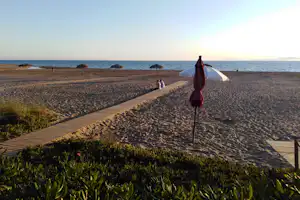 Holzsteg am Strand mit Sonnenschirmen, Blick aufs Meer und zwei Personen am Abendhimmel.