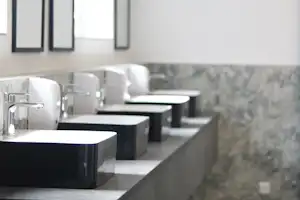 Mehrere Waschbecken in einem modernen Sanitärbereich, mit Spiegeln, Armaturen und grauen Fliesen an der Wand.
