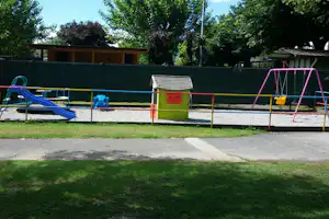 Spielplatz auf dem Campingplatz: bunte Rutsche, Schaukel und Sandkasten vor Hecken und Bäumen.