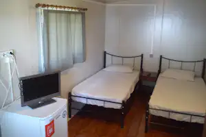 Schlafzimmer mit zwei Betten, Vorhang am Fenster, TV auf dem Schrank und Steckdose an der Wand.