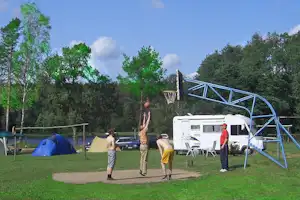 Campingplatz mit Zelt, Wohnmobil und Basketballkorb auf Rasen, daneben Sitzgruppe und Autos am Stellplatz.