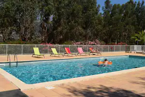 Schwimmbad mit türkisfarbenem Wasser, mehreren Liegestühlen am Beckenrand und Bäumen im Hintergrund.