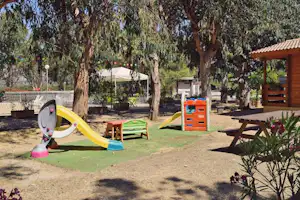 Spielbereich mit Rutsche und Kletterwand auf dem Campingplatz, daneben Gartenmöbel und ein Holzpavillon im Schatten der Bäume.