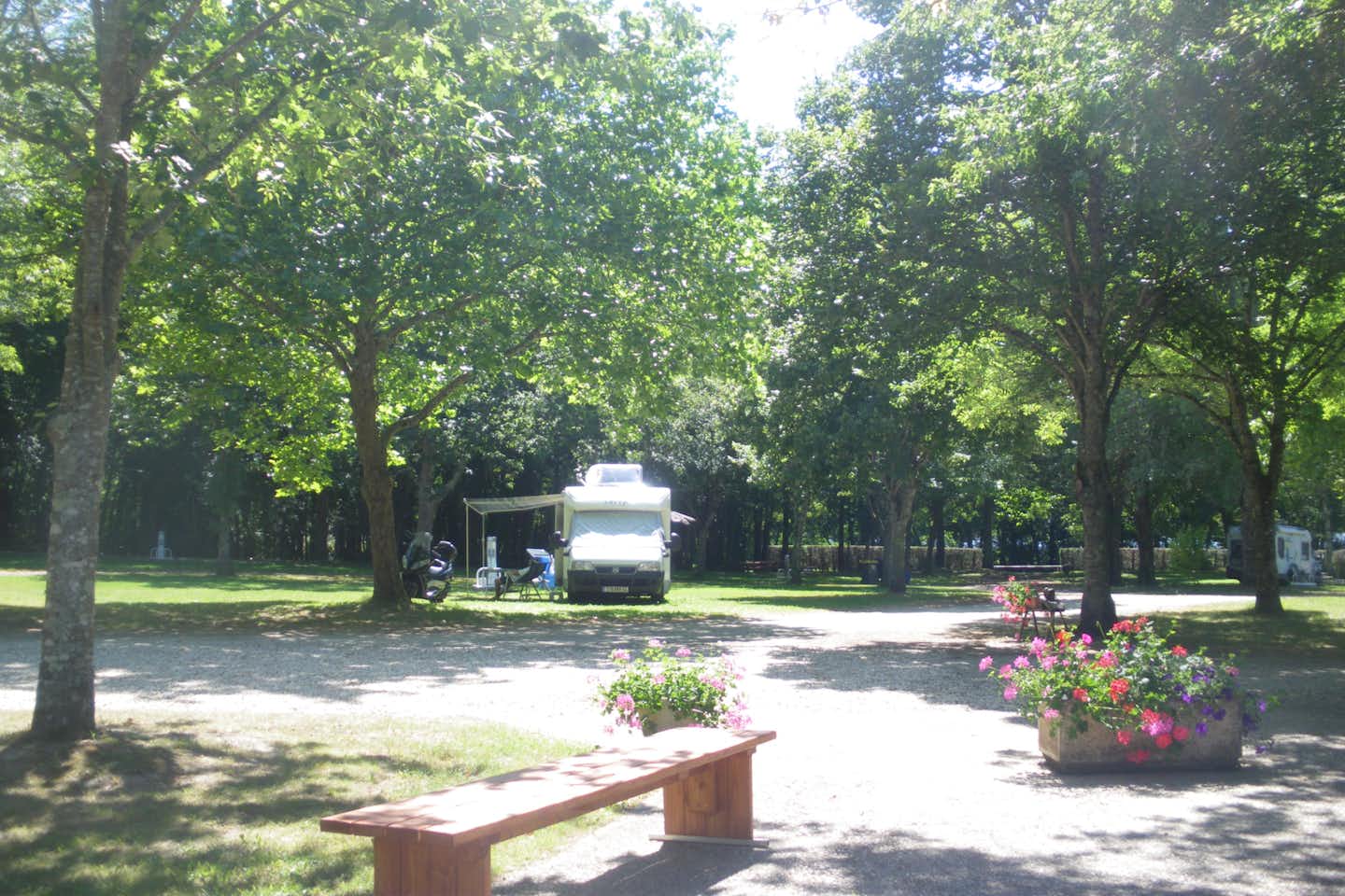 Camping Paradis de la Nature - Stellplätze mit einzelnem Mobilheim mit Vorzelt, im Vordergrund eine Bank und Blumenbeet