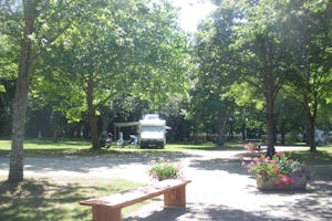 Camping Paradis de la Nature - Stellplätze mit einzelnem Mobilheim mit Vorzelt, im Vordergrund eine Bank und Blumenbeet