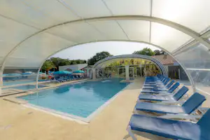 Überdachtes Schwimmbecken mit Liegestühlen im Campingbereich, transparente Zeltwände und Poolrand aus Beton.