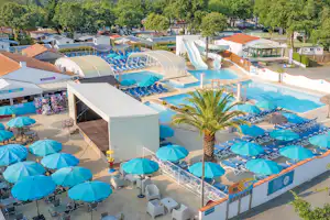 Großer Campingpool mit blauen Liegen und Sonnenschirmen, daneben Wohnwagen und Zelte im Ferienpark.