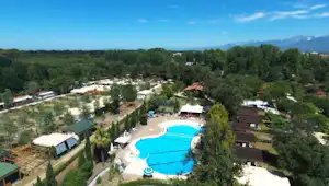 Luftaufnahme eines Campingplatzes mit großem Pool, mehreren Stellplätzen, Wegen und Bungalows inmitten von Bäumen und Grünflächen.
