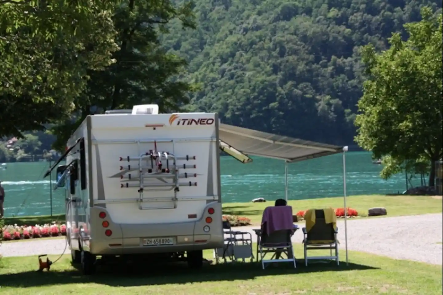 Camping Paradiso Lago - Camper sitzt unter der Markise eines Wohnmobils mit Blick auf den Luganersee