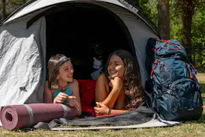 Campingzelt im Wald, zwei Personen sitzen im Zelt, Rucksack und Isomatte liegen davor.