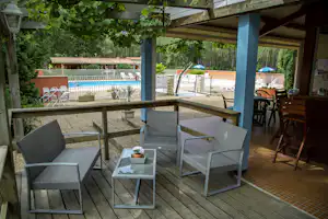 Sitzgruppe auf der Camping-Terrasse unter einem Dach, mit Tisch, Stühlen und Blick auf den Poolbereich und Bäume.