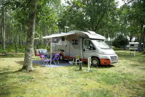 Wohnmobil auf einem Campingplatz im Grünen, mit Vorzelt, Campingstühlen und Tisch zwischen Bäumen.