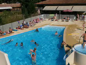 Großes Camping-Schwimmbecken mit Rutsche, Gäste im Wasser und am Beckenrand, im Hintergrund Gebäude und Bäume.