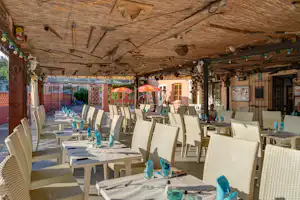 Speisebereich im Campingplatz: gedeckte Tische mit weißen Stühlen unter einer Holzdecke, im Hintergrund Türen und Fenster.