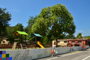 Großer Baum vor Campinggebäuden, im Vordergrund eine bunte Mauer und ein Schild „Reception“.