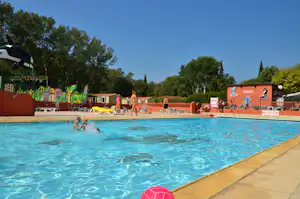 Schwimmbecken auf dem Campingplatz mit Kindern im Wasser, Liegen am Beckenrand und Spielbereich mit Rutsche.