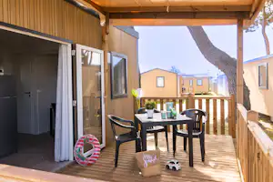 Holz-Terrasse am Wohnwagen mit Tisch und Stühlen unter Überdachung, daneben Spielzeugauto und bunte Tasche.