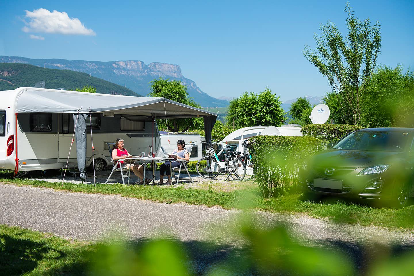 Camping-Park Steiner - Camperpaar vor ihrem Wohnwagen in der Sonne Blick auf die Alpes  