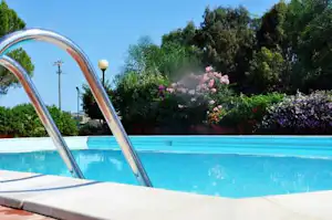 Campingpool mit Treppe aus Metall, umgeben von Blumenbeeten und Bäumen im Hintergrund.