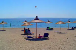Camping-Sitzgruppe mit Sonnenschirmen am Strand, Liegen und Stühle vor dem Meer.