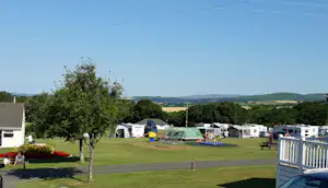 Campingplatz mit Wohnwagen und Zelten auf dem Stellplatz, Rasenfläche, Bäume und Blick auf die Hügel in der Ferne.