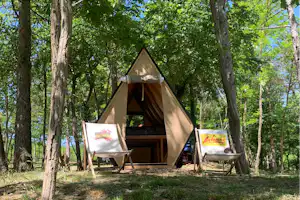 Campingzelt im Wald mit zwei Klappstühlen und offenem Eingang, umgeben von Bäumen und Gras am Stellplatz.