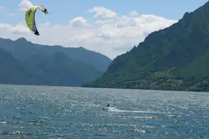 Kitesurfer auf dem See mit grünem Bergpanorama und Drachen im Himmel.