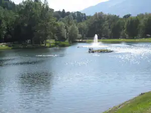Blick auf einen Campingsee mit Fontäne, Ruderbooten und grünen Bäumen am Ufer.