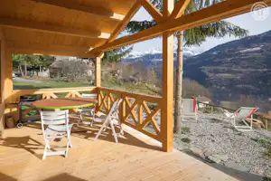 Holzterrasse mit Tisch und Stühlen unter einem Carport, Blick auf Berge und Skigebiet, Liegestühle am Rand.