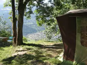 Campingzelt am Waldrand im Grünen, mit Bäumen und Blick auf eine hügelige Landschaft im Hintergrund.