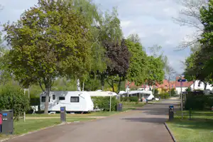 Wohnmobil auf einem Stellplatz zwischen Bäumen, mit weiteren Wohnwagen und einem Weg im Campinggelände.