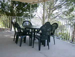 Terrasse mit mehreren Gartenstühlen aus Kunststoff und Geländer, dahinter Bäume und grünes Umfeld.