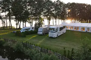 Mehrere Wohnmobile auf einem grünen Campingplatz, umgeben von Bäumen und einem gepflegten Rasen.