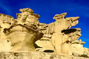 Felsformation aus hellem Gestein mit markanten Ausbuchtungen vor blauem Himmel, Nahaufnahme einer natürlichen Felswand.