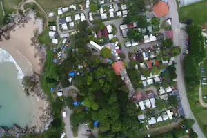 Luftaufnahme eines Campingplatzes mit vielen Stellplätzen, Wohnwagen und Zelten am Flussufer, umgeben von Bäumen und Wegen.