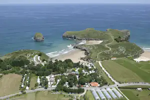 Campingplatz an der Küste, Luftaufnahme mit Strand, Wegen, Wiesen und Bäumen sowie Felsen im Meer.