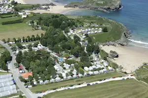Luftaufnahme eines Campingplatzes mit Stellplätzen, Wohnwagen und Zelten nahe dem Strand und dem Meer.