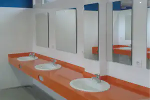 Waschbecken mit Armaturen auf orangefarbener Waschtischplatte, dazu Spiegel und weiße Fliesen im Camping-Badezimmer.