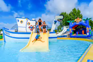 Kinder auf einer Wasserrutsche im Schwimmbecken, aufblasbares Spielgerät mit Rutsche und Spritzschutz vor blauem Himmel.