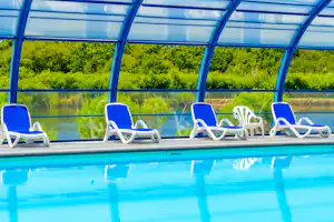 Blaue Pool-Liegen unter einer transparenten Überdachung am Schwimmbecken, im Hintergrund grünes Ufer und Wasser.