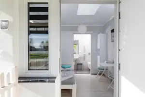 Offene Tür zum Badezimmer im Camping-Bungalow: weiß gefliester Raum, Waschbecken, Toilette und Fensterblick ins Grüne.