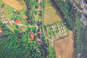Luftaufnahme einer Campinganlage mit Stellplätzen, Wegen, Gebäuden und vielen Bäumen im grünen Waldgebiet.