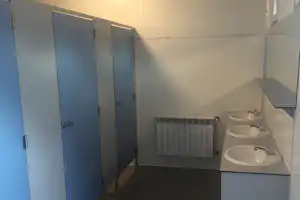 Badezimmer im Campingbereich mit zwei Waschbecken, Heizkörper und mehreren Türen, hell gefliest und mit Ablage.