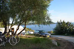 Campingplatz mit Wohnmobil und Auto am Weg, Olivenbäume im Vordergrund, Blick auf das Meer und die Küste.